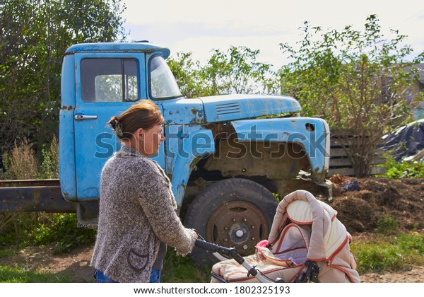 mother with stroller
and old car,mom with a stroller on the background of a broken old
truck in the village