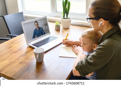 Mother Is Studying Online, Watching Webinars While Staying At Home With Child. Mom Looks At Laptop Screen And Writes, Kid Sits On Her Laps