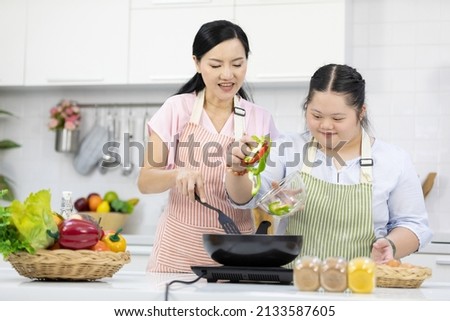 mother support down syndrome teenage girl or her daughter cooking food and frying pan on kitchen table