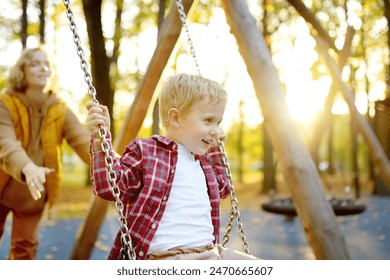 A mother swings her son on a swing in an autumn city park. A beautiful woman entertains her adorable baby on the playground. Traditional active seasonal entertainment for families with children - Powered by Shutterstock