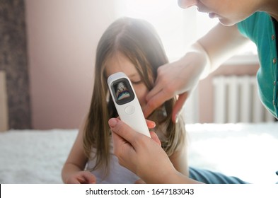 Mother takes temperature for her child with infrared thermometer at home. Mother hand holding digital infrared thermometer.