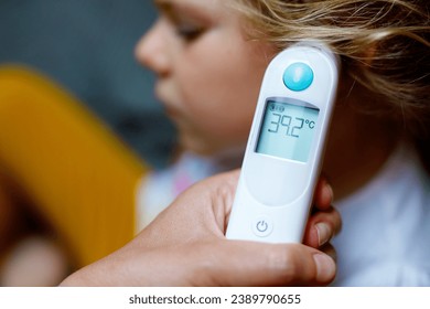 Mother takes temperature for her little preschool daughter, sick child with infrared in ear thermometer at home, high grade fever Mother hand holding digital infrared thermometer. - Powered by Shutterstock