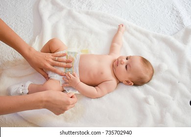 Mother taking care of little girl. Mom giving baby a diaper change on bed.
