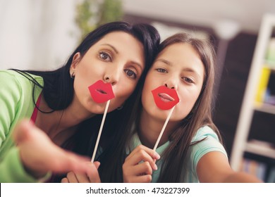Mother Taking Selfie With Daughter Holding Artificial Lips Stick At Home