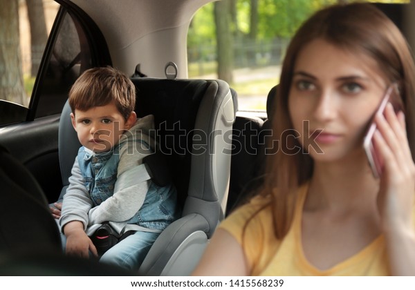 Mother talking by phone while driving car with\
her son on backseat. Child in\
danger