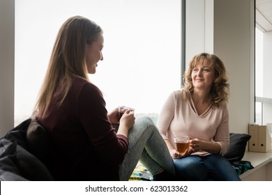 Mãe conversando com a filha enquanto toma chá em casa
