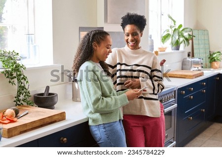 Mother Talking With Teenage Daughter At Home As She Checks Social Media On Mobile Phone