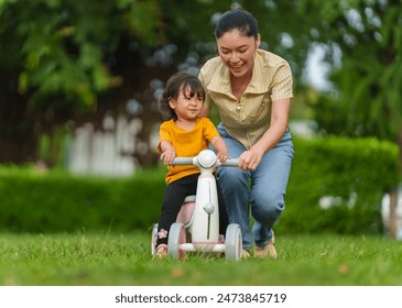 mother teaches her baby toddler girl rides a plastic motorcycle toy in the park - Powered by Shutterstock