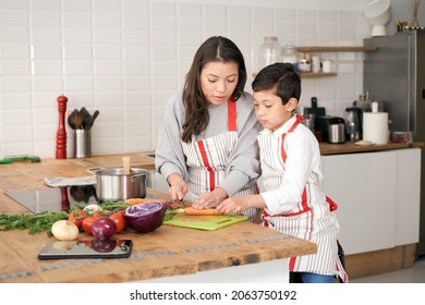 Mother Teaches Her Son How To Cook Healthy Food In The Kitchen. Lifestyle With Latino People In Single Parent Family. Child Learning To Cook.