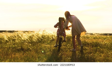mother teaches little child daughter ride bike park sunset. cycling kid with parent outdoors. happy family. mother daughter play with bicycle nature. happy family concept. chidhood dream. weekend.
