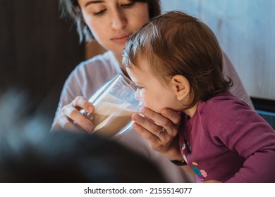 Mother Teaching Baby Girl To Drink From Glass. Woman Helping Child Drinking Milk. Baby Care.