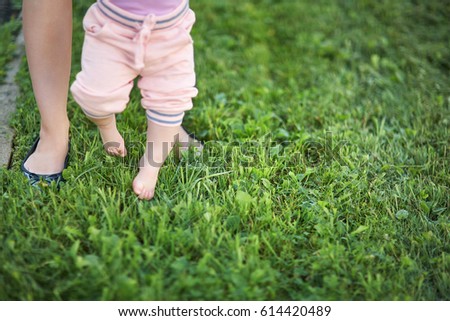 Mother teaching her baby to take the first steps barefoot on the grass
