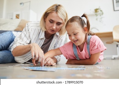 Mother teaching her daughter with down syndrome collecting puzzles they lying on the floor in the room - Shutterstock ID 1789915070