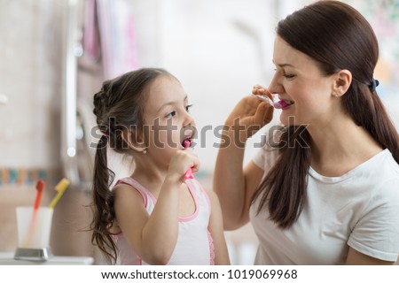 mother teaching kid daughter teeth brushing in bathroom