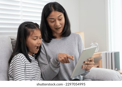 Mother teaching lesson for daughter by tablet. Mother and child smile happily together. Do homework with kind mother help, encourage for exam. Asia girl happy Homeschool. Mom advise education together - Powered by Shutterstock