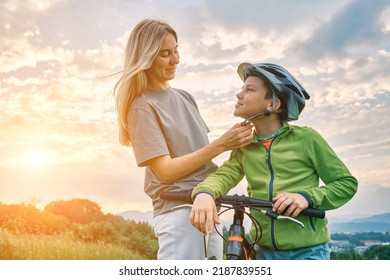 Mother Teaching Son To Ride Bicycle. Happy Cute Boy In Helmet Learn To Riding A Bike In Park On Green Meadow In Summer Day At Sunset Time. Family Weekend. 4K Video Slow Motion