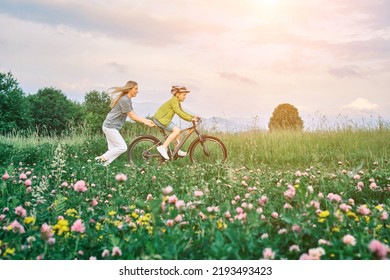 Mother Teaching Son To Ride Bicycle. Happy Cute Boy In Helmet Learn To Riding A Bike In Park On Green Meadow In Summer Day At Sunset Time. Family Weekend. 4K Video Slow Motion