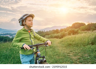 Mother Teaching Son To Ride Bicycle. Happy Cute Boy In Helmet Learn To Riding A Bike In Park On Green Meadow In Summer Day At Sunset Time. Family Weekend. 4K Video Slow Motion