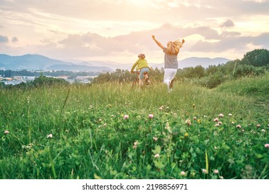 Mother Teaching Son To Ride Bicycle. Happy Cute Boy In Helmet Learn To Riding A Bike In Park On Green Meadow In Summer Day At Sunset Time. Family Weekend. 4K Video Slow Motion