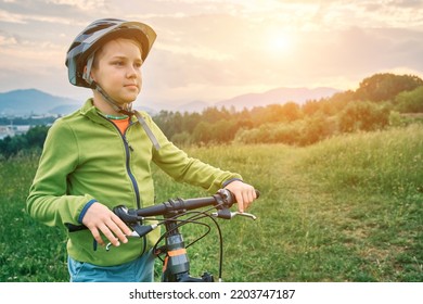 Mother Teaching Son To Ride Bicycle. Happy Cute Boy In Helmet Learn To Riding A Bike In Park On Green Meadow In Summer Day At Sunset Time. Family Weekend. 4K Video Slow Motion