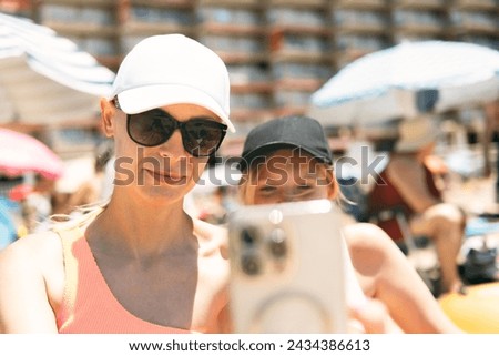A mother and teenage daughter, both in swimsuits, capture a selfie against the backdrop of a sunny beach, epitomizing summer bonding and fun i Stock photo © 
