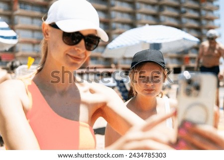 A mother and teenage daughter, both in swimsuits, capture a selfie against the backdrop of a sunny beach, epitomizing summer bonding and fun i Stock photo © 