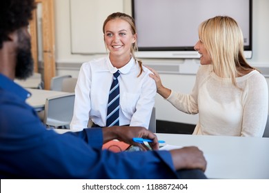 Mother And Teenage Daughter Having Discussion With Male Teacher At High School Parents Evening