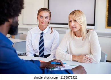 Mother And Teenage Daughter Having Discussion With Male Teacher At High School Parents Evening