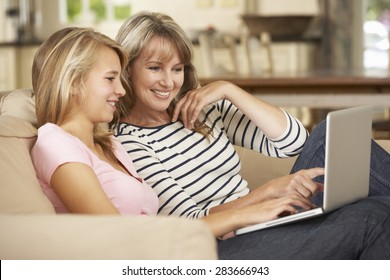 Mother With Teenage Daughter Sitting On Sofa At Home Using Laptop