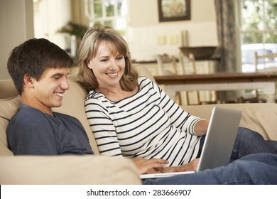 Mother With Teenage Son Sitting On Sofa At Home Using Laptop