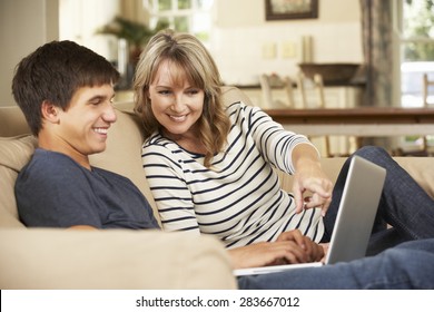 Mother With Teenage Son Sitting On Sofa At Home Using Laptop