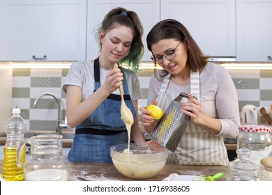 Mother and teenager daughter cook together at home in kitchen. Girl helps her mom stir dough, woman rubs lemon zest. Parent teen communication, family, mothers day