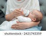 Mother tenderly feeds newborn with milk formula, Concept of modern parenting and nourishment