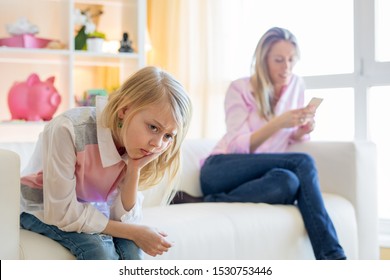 Mother is texting while her little girl  unhappy sitting next to her on couch