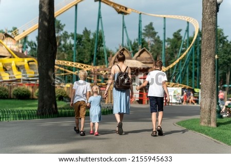 Mother with three children goes to an amusement park. Back view. Family goes to riding the roller coaster