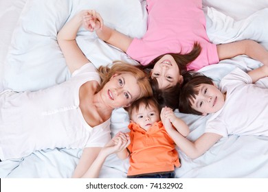 Mother And Three Kids Lying On Bed And Holding Hands