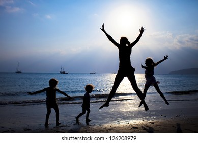 Mother And Three Kids Silhouettes Jumping On Beach At Sunset