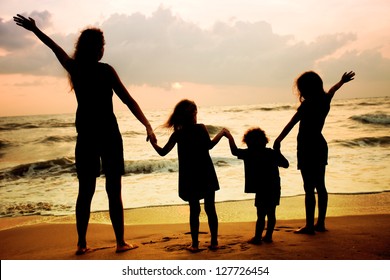 Mother And Three Kids Silhouettes Standing On Beach At Sunset