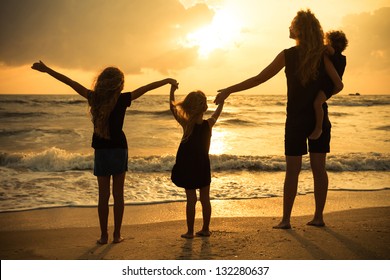 Mother And Three Kids Silhouettes Standing On Beach At Sunset