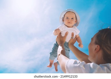 Mother Throwing Baby Up Against The Blue Sky. Happy Family Outdoors. Mom And Baby At Summer On Nature. Positive Human Emotions And Feelings.