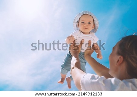 Mother throwing baby up against the blue sky. Happy family outdoors. Mom and baby at summer on nature. Positive human emotions and feelings.