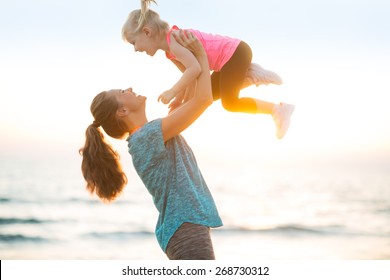 Mother Throwing Baby Up On Beach In The Evening