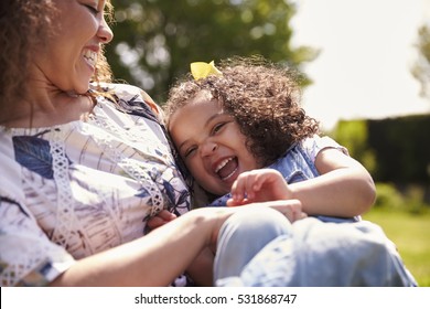 Mother tickling her daughter, sitting in a garden