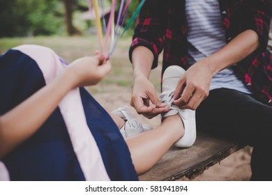 Mother tied shoe for her daughter while sitting on swing relaxing out doors together.