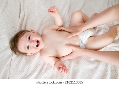 A mother with a toddler baby does gymnastics, children sports and fitness classes at home. Woman mom and child do morning exercises lying on the bed. Kid aged one year - Powered by Shutterstock