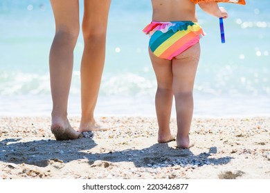 Mother And Toddler Child Baby Girl Chubby Legs Walking At Sea Beach With Colorful Pop It Toy, Family Vacation