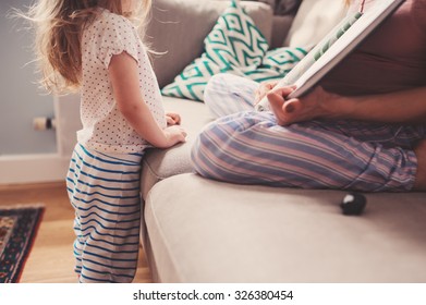 Mother And Toddler Daughter Reading Book At Home