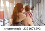 Mother and toddler daughter walk together on passage boarding plane. Brown-haired woman prepares for coming back to hometown with girl on airplane, sunlight