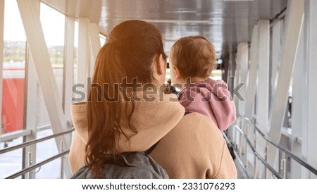 Mother and toddler daughter walk together on passage boarding plane. Brown-haired woman prepares for coming back to hometown with girl on airplane, sunlight