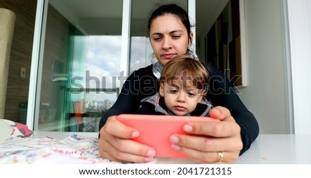 Mother and toddler watching online content on cellphone. Parent and child boy using smartphone
